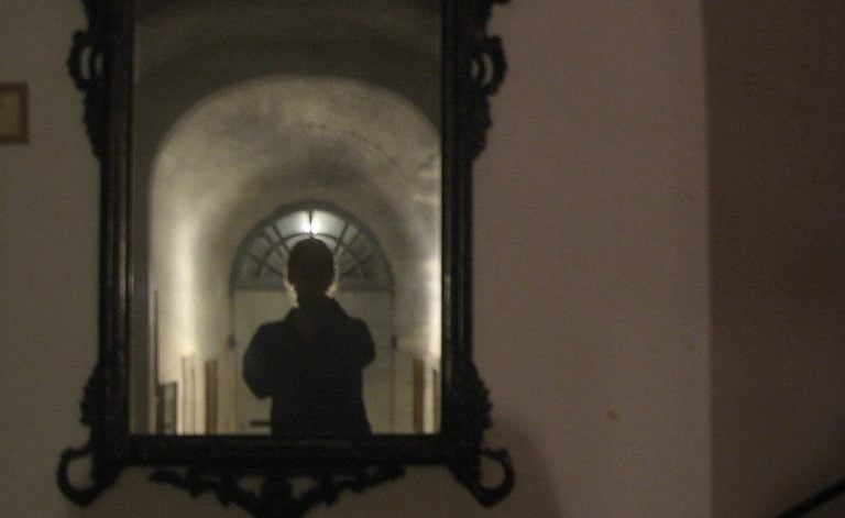 A shadowy figure in a mirror, invoking the haunting nature of Bloody Mary