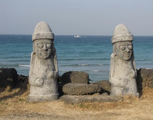 Twin Dol Hareubang statues set against a garden background.