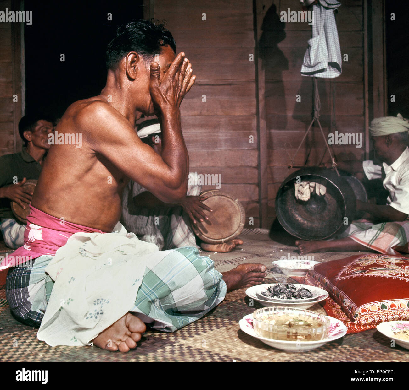 A bomoh practicing traditional treatments with herbs in a sacred environment.